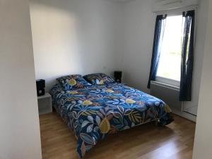 Un dormitorio con una cama con un edredón colorido y una ventana en Appartement + Jardin, en Fouesnant