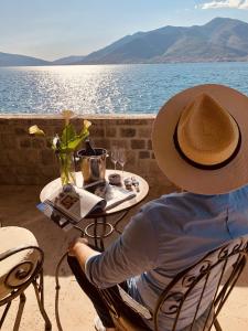 Un uomo con un cappello seduto a un tavolo vicino all'acqua di Eco Hotel Carrubba a Tivat