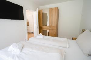 2 weiße Betten in einem Zimmer mit einem Flachbild-TV in der Unterkunft Apartments Oasis Wörthersee neu & zentral in Krumpendorf am Wörthersee