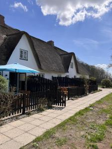 a white house with a fence and an umbrella at Moorhuus - Paradies am Wilden Moor in Winnert