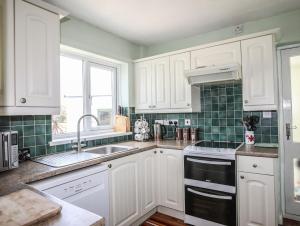 a kitchen with white cabinets and a sink and a window at Anwylfa in Moelfre