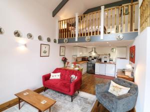 a living room with a red couch and chairs and a kitchen at Wisteria Cottage in Paignton