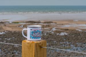 a coffee mug sitting on top of a wooden post near the beach at No.1 The Prom in Westward Ho