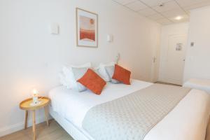um quarto com uma cama branca com almofadas laranja e azul em Hôtel Porte Mars Reims Gare Centre Arena em Reims