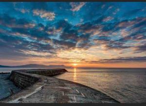a sunset over the water near a pier at Large property which is all about location, location , location ! Lovely Comfortable 2 bedroom flat which is spacious and one of the best value properties of this size so close to the sea , beaches and restaurants 1 min to the sea ! in Lyme Regis