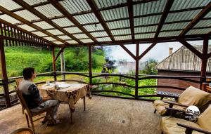 un hombre sentado en una mesa en un porche con vistas en Pensiunea Barsan, en Vişeu de Sus