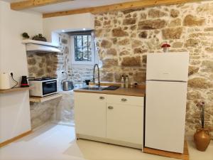 cocina con armarios blancos y pared de piedra en Zaira's Apartment Corfu Town, en Ágios Rókkos