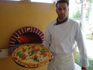 a man holding a pizza in front of a pizza oven at Vergos Hotel in Vourvourou