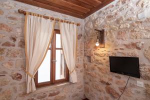 a stone walled room with a window and a television at Aeolos Guesthouse in Monemvasia