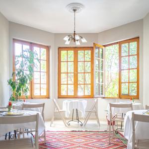 a dining room with white tables and chairs and windows at Garden Boutique B&B in Tirana