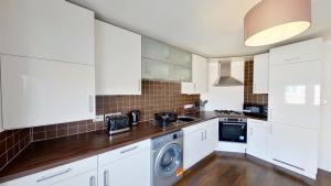 cocina con armarios blancos, lavadora y secadora en Orange Apartments Bothwell Road, en Aberdeen