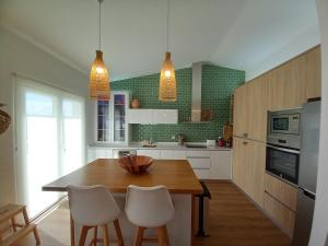 a kitchen with a wooden table and white chairs at SARDINHA BOÉMIA SUDOESTE By Stay In Alentejo in Fataca