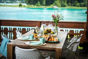 una mesa de madera con comida y bebida y vistas al lago en Ferienhaus Faakersee Hideaway am See, en Faak am See