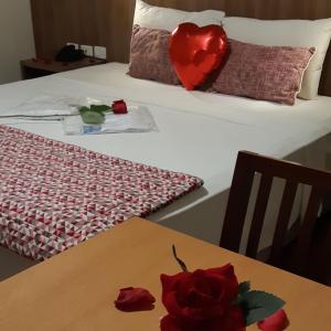 ein Bett mit einem Herzkissen und einem Tisch mit Rosen in der Unterkunft Comfort Mogi Guaçu in Mogi-Guaçu