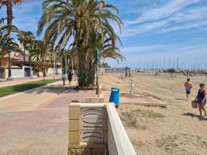 una playa con palmeras y gente caminando por la arena en Precioso apartamento residencial con vistas al mar, en La Pobla de Farnals