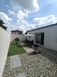 een patio met een tafel en stoelen en een parasol bij Charmante maison aux portes de la Rochelle in La Jarrie