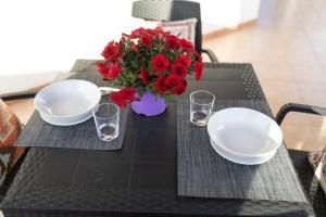 a table with two plates and a vase of red flowers at MrBrown - Cinzia Resort Beach in Mazara del Vallo