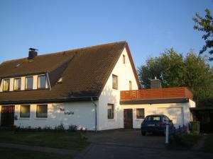 une maison blanche avec une voiture garée devant elle dans l'établissement Haus-Halligblick-Ferienwohnung-Pellworm, à Dagebüll