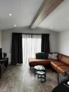 sala de estar con sofá marrón y ventana grande en Polderhuisje 2 - Heerlijk chalet met overkapt terras en 2 slaapkamers - max 4 pers - 3 km van Noordzee - locatie op camping 2, en Rockanje