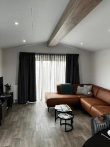 a living room with a brown couch and a large window at Polderhuisje 2 - Heerlijk chalet nabij strand en duin - 2 slaapkamers - Midicamping - Rockanje in Rockanje
