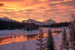 a sunset over a river in the snow with mountains at Mount Robson Inn in Jasper