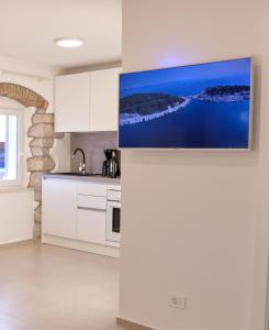 a kitchen with white cabinets and a tv on the wall at Apartment House Bucul in Mali Lošinj