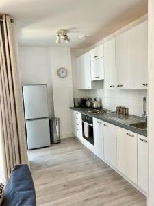 2 Bedroom Serviced Apartment with Free Parking, Wifi & Netflix, Basingstoke في باسينغستوك: مطبخ مع دواليب بيضاء وثلاجة