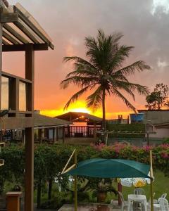 um pôr-do-sol num resort com uma palmeira e um guarda-sol em Pousada Do Sol em Conceição da Barra