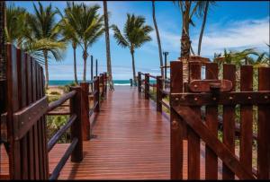 a wooden boardwalk leading to the beach with palm trees at Vivant Eco Resort apartamento in Barra Grande