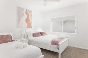 a white bedroom with two beds and a window at HideAway I at Shoal Bay in Shoal Bay
