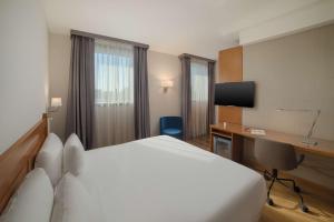a hotel room with a bed, desk, chair and a television at NH Ravenna in Ravenna