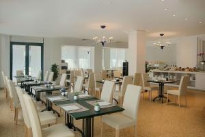 une salle à manger avec de longues tables et des chaises blanches dans l'établissement NH Ravenna, à Ravenne