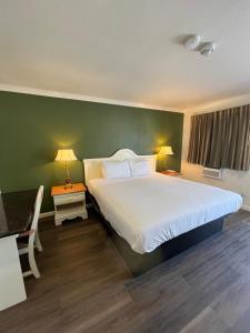 - une chambre avec un grand lit blanc et un mur vert dans l'établissement American Inn - Grover beach - Pismo Beach, à Grover Beach
