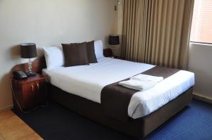 a hotel room with a bed and a phone on a night stand at City Park Hotel in Melbourne
