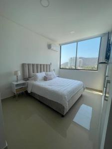 Dormitorio blanco con cama y ventana grande en Apartamento en Santa Marta - Samaria club de playa, en Santa Marta