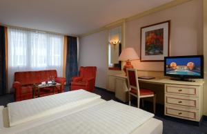 バート・ゲーグギングにあるThe Monarch Hotelのベッド、デスク、テレビが備わるホテルルームです。