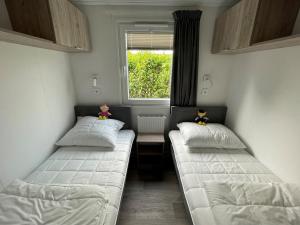 two beds in a small room with a window at Polderhuisje 2 - Heerlijk chalet nabij strand en duin - 2 slaapkamers - Midicamping - Rockanje in Rockanje