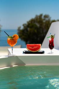two cocktails and a slice of watermelon on a table by a pool at Seaside Breeze in Kamari