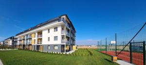 a white building with a fence next to a tennis court at COSTA Apartamenty w Sarbinowie in Sarbinowo