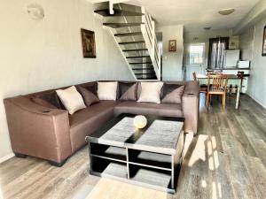 a living room with a brown couch and a staircase at 39 Settler Sands Beachfront Accommodation Sea and River View in Port Alfred
