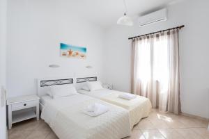 a white bedroom with two beds and a window at Eleftheria Hotel & Apartments in Ornos