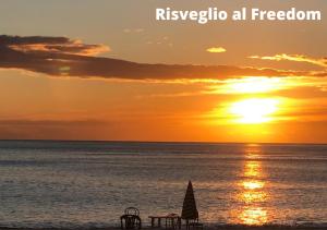 a sunset on the beach with a table and an umbrella at Freedom Village in Soverato Marina