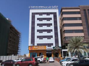 ein hohes Gebäude mit Autos auf einem Parkplatz in der Unterkunft OYO 109 Al Thabit Modern Hotel Apartment in Ḩayl Āl ‘Umayr