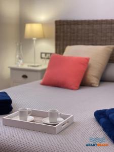 a tray with two cups on a bed with a red pillow at APARTBEACH PANORAMIC VISTAS PLAYA y PISCINA in Miami Platja