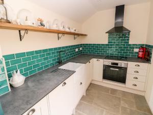 a kitchen with white cabinets and green subway tiles at Lime Kiln Cottage in Bridgend