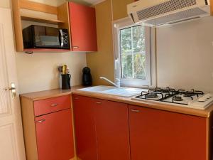 a kitchen with red cabinets and a stove and a window at Logement 2 chambres avec jacuzzi sur terrain en pleine nature in Beaucaire