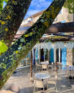 a tree with tables and chairs in front of a building at Hotel Le Provence - Restaurant Le Styx in La Palud-sur-Verdon