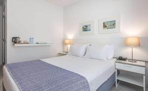 a white bedroom with a large bed and a nightstand at Hotel Baltum in Albufeira