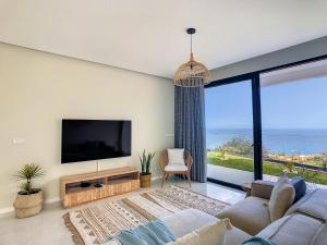 ein Wohnzimmer mit einem TV und einem großen Fenster in der Unterkunft Noah - Private Sunset Hideaway by LovelyStay in Arco da Calheta