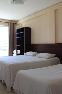two beds in a hotel room with a window at Tropical Palace Hotel in Lavras